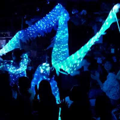 People at a dim party holding glowing blue LED light ropes/or ribbons, creating a neon scene in the dark room.